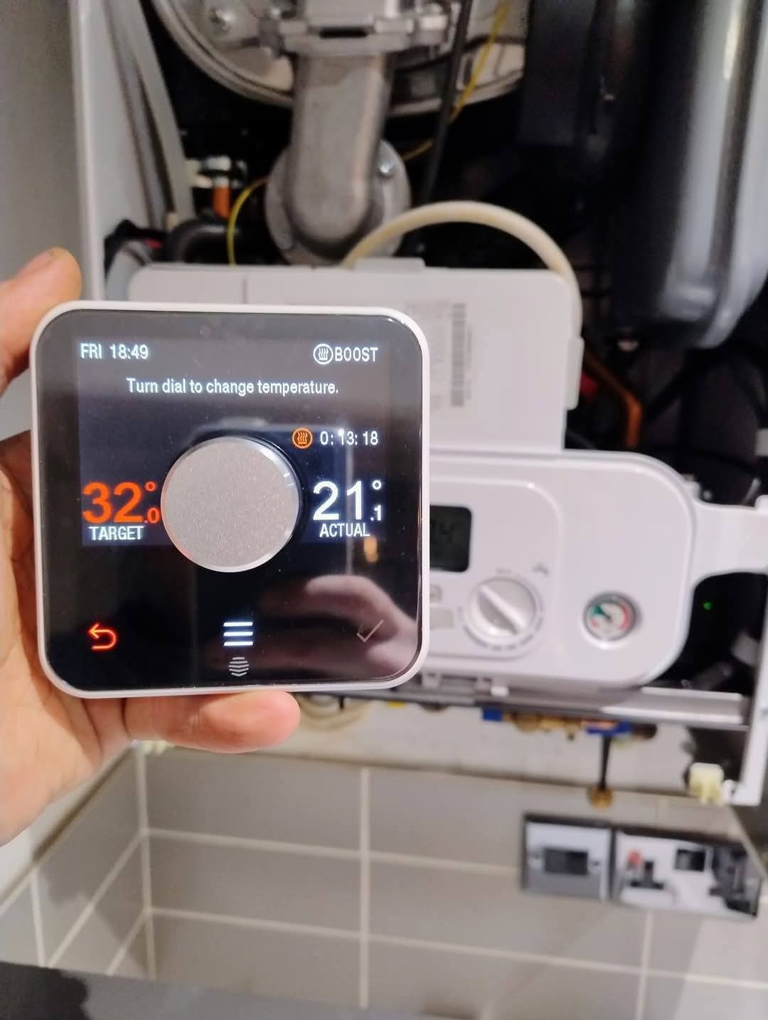 A Hive smart thermostat set up in front of an open boiler